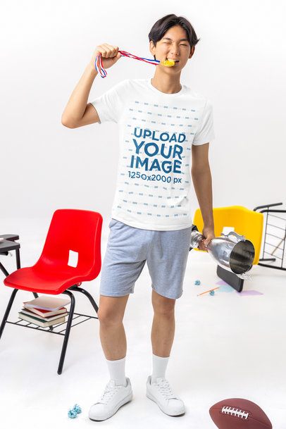 Bella Canvas T-Shirt Mockup of a Young Man Holding a Trophy and Biting a Medal in a Classroom Set