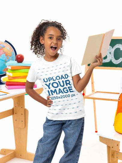 Bella Canvas Tee Mockup of a Surprise Girl Holding a Notepad in a Classroom Setting