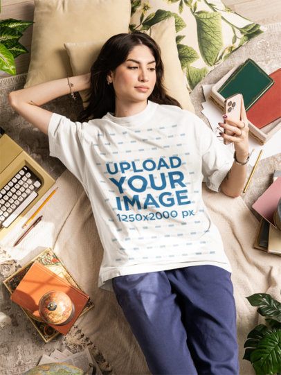 Oversized T-Shirt Mockup Featuring a Woman Relaxing in a Comfy Setting With a Smartphone