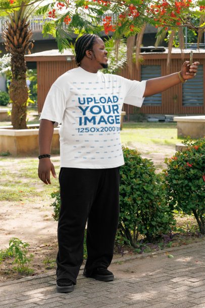 Oversized T-Shirt Mockup Featuring a Smiling Man Taking a Selfie in a Park