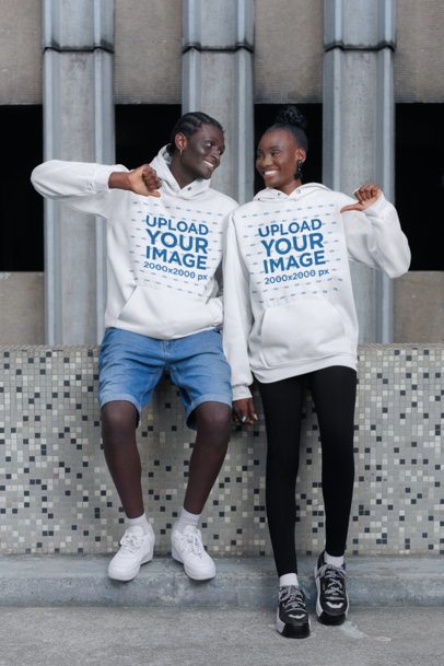 Mockup Featuring a Smiling Man and a Woman Pointing at Their Pullover Hoodies in the Street