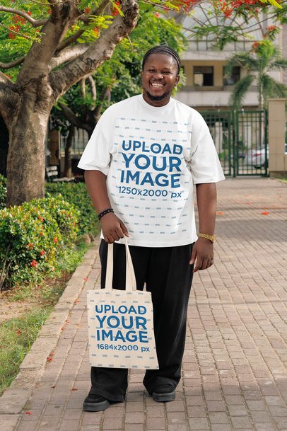 Oversized T-Shirt Mockup Featuring a Cheerful Man Walking in the Street With a Tote Bag