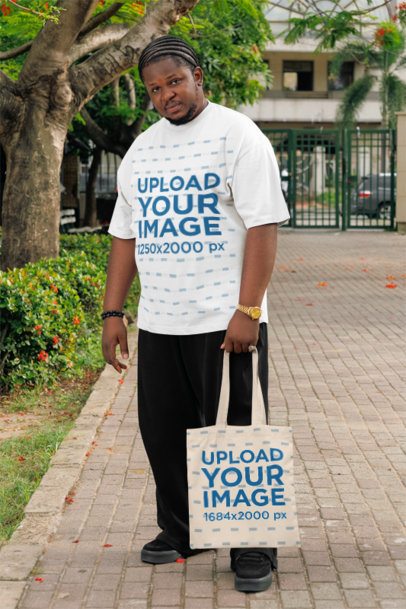 Oversized T-Shirt Mockup Featuring a Serious Man Standing in the Street With a Tote Bag