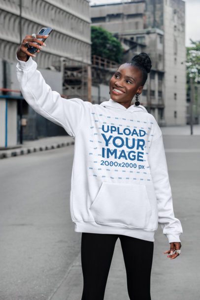 Oversized Hoodie Mockup Featuring a Cheerful Woman Taking a Selfie on the Sidewalk