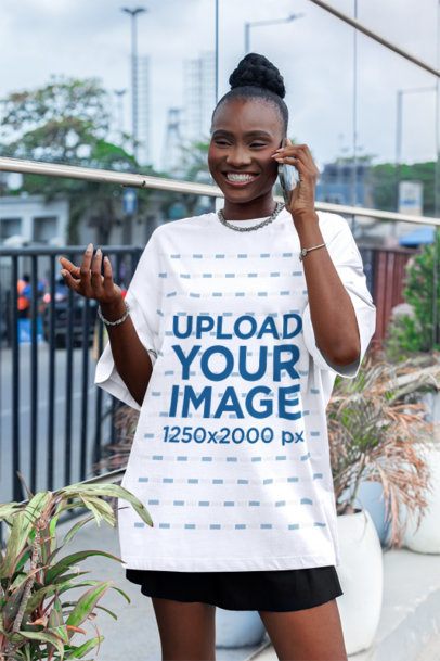 Oversized T-Shirt Mockup Featuring a Cheerful Woman Talking on the Phone in the Street