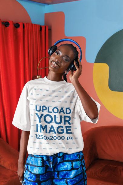 Oversized T-Shirt Mockup Featuring a Happy Woman Listening to Music in an Artsy Living Room