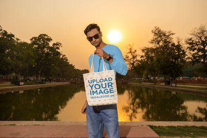Tote Bag Mockup Featuring a Man Posing in a Park With a Lake and a Nice Sunset  m56805