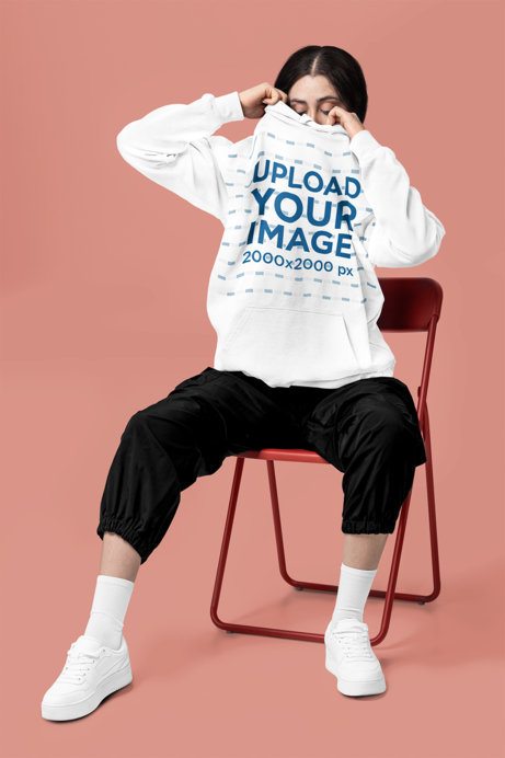 Comfort Colors Mockup Featuring a Woman Covering Her Face With a Hoodie While Sitting on a Chair