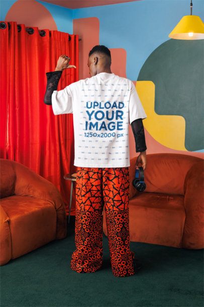 Back-View Mockup Featuring a Man Pointing at His Oversized T-Shirt in a Colorful Living Room