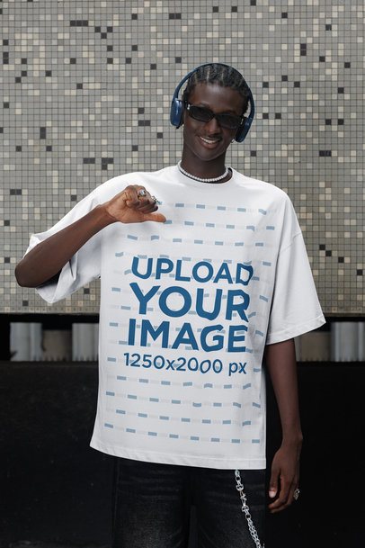 Mockup Featuring a Cheerful Man With Headphones Pointing at His Oversized Tee in the Street