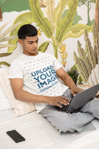T-Shirt Mockup of a Man Resting on a Cozy Bed While Checking His Laptop m55421
