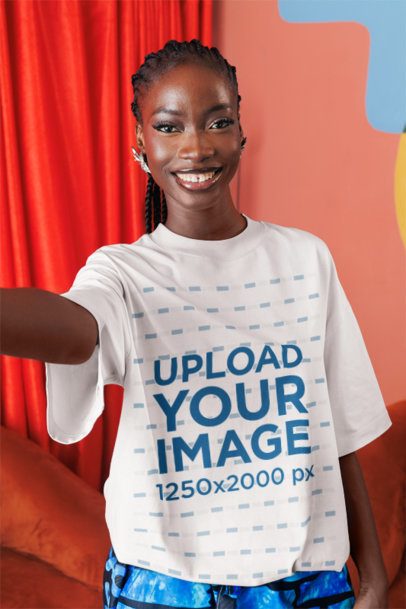Oversized T-Shirt Mockup of a Joyful Woman Taking a Selfie in a Colorful Living Room