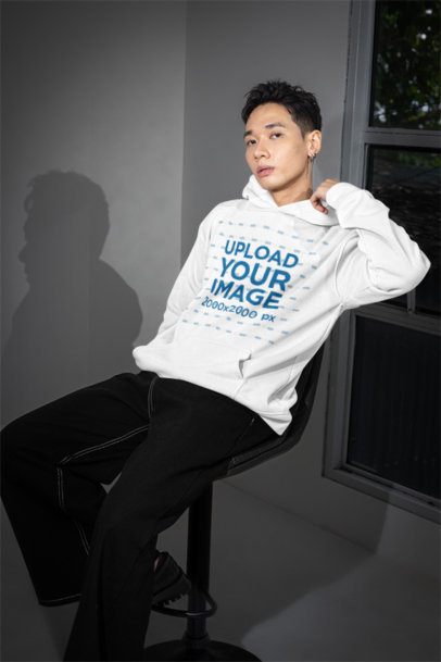 Pullover Hoodie Mockup Featuring an Alternative-Styled Man Sitting on a Chair Near a Window m54169