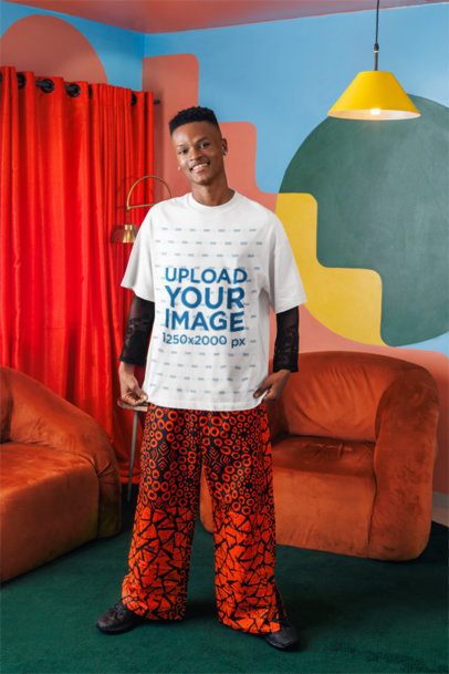 Oversized T-Shirt Mockup Featuring a Happy Young Man Posing in a Colorful Living Room