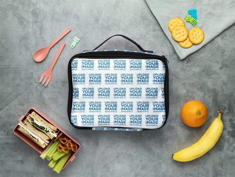 Mockup Featuring a Lunch Bag Placed on a Surface Surrounded by Snacks and Fruits