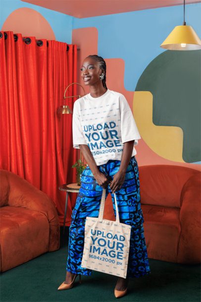 Oversized T-Shirt Mockup of a Cheerful Woman Posing With a Tote Bag in a Colorful Living Room