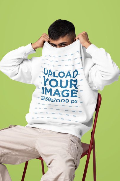 Mockup of a Man Covering His Face With a Comfort Colors Sweatshirt While Sitting on a Chair in a Studio m57428