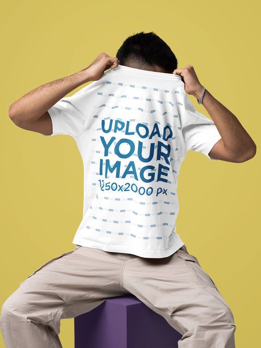 Oversized T-Shirt Mockup Featuring a Man Covering His Face While Sitting on a Cube in a Studio