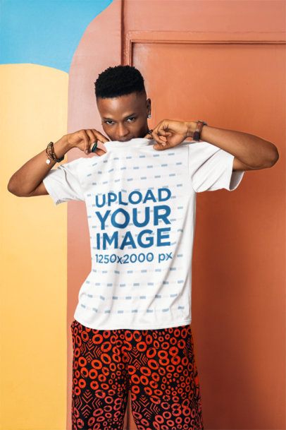 Mockup Featuring a Man Biting the Round-Neck of His T-Shirt While Posing Against an Artsy Wall