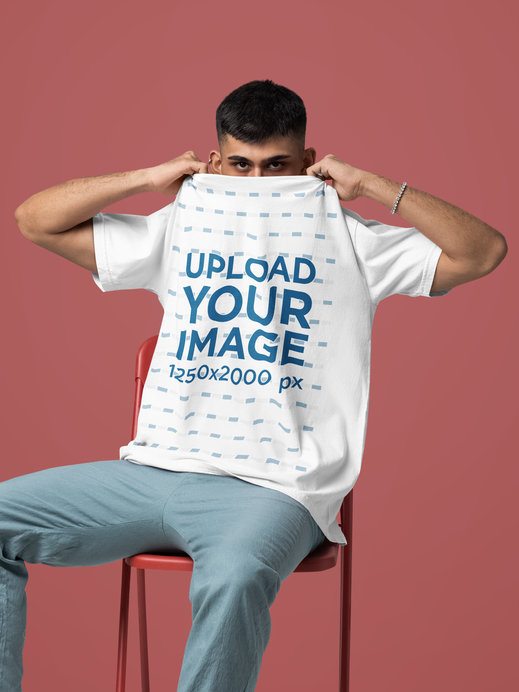 Comfort Colors T-Shirt Mockup Featuring a Man Covering His Face While Sitting on a Chair in a Studio