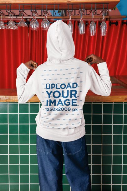 Back-View Mockup of a Woman Pointing at Her Pullover Hoodie in a Bar