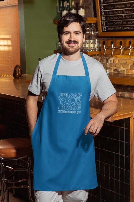 Apron Mockup Featuring a Smiling Bearded Man Posing in a Bar