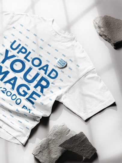 Mockup of an Oversized T-Shirt and a Pin Lying on a Surface With Rocks m58149