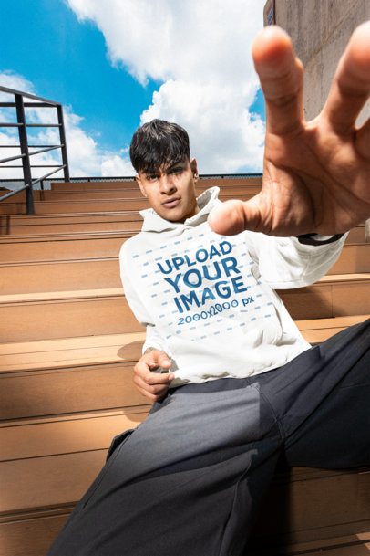 Comfort Colors Hoodie Mockup of a Man Reaching His Hand to the Camera While Seated on the Bleachers m57615