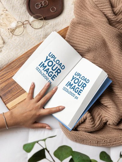 Mockup Featuring a Woman's Hand Holding an Open Book in a Cozy Bed