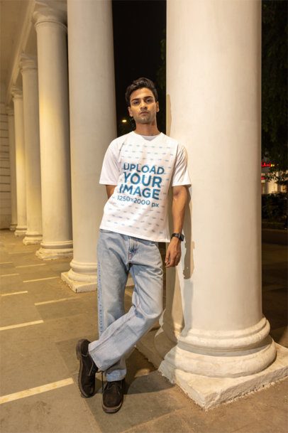 Oversized T-Shirt Mockup Featuring a Man Leaning on a Pillar in the Street