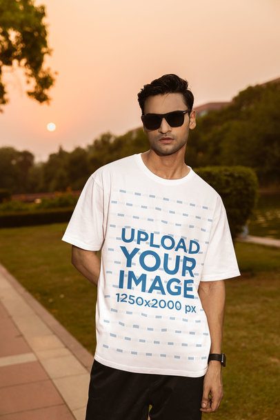 Oversized T-Shirt Mockup of a Man Posing in a Park at Sunset