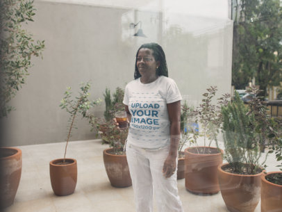 Through-the-Window T-Shirt Mockup of a Lady with Small Braids Next to Plant Pots 21413