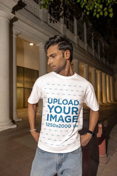 Oversized T-Shirt Mockup of a Man Posing in the Street Near a Building at Night