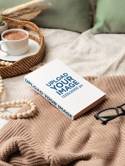 Mockup of a Paperback Book Lying on a Bed With a Chocolate Cup