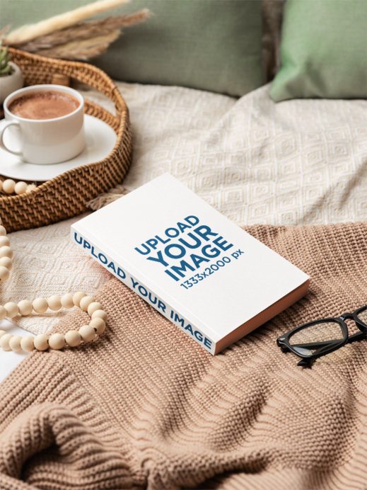 Mockup of a Paperback Book Lying on a Bed With a Chocolate Cup