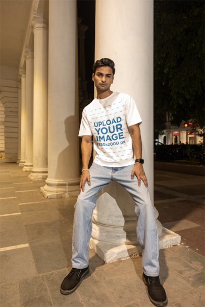Oversized T-Shirt Mockup of a Man Standing Against a Pillar in the Street