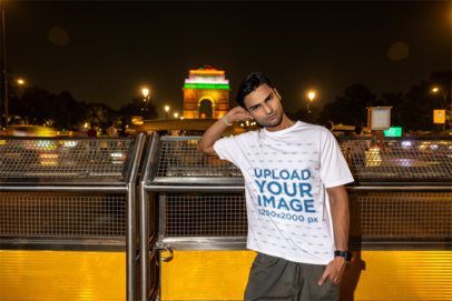 Oversized T-Shirt Mockup Featuring a Serious Man Posing on a Bridge in a City at Night