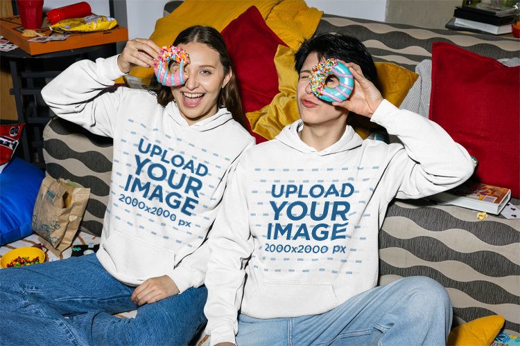 Comfort Colors 1567 Hoodie Mockup Featuring a Man and a Woman Posing With Donuts in a Living Room