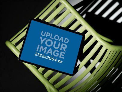 Mockup of an iPad Resting on a Green Abstract Chair in a Dark Studio