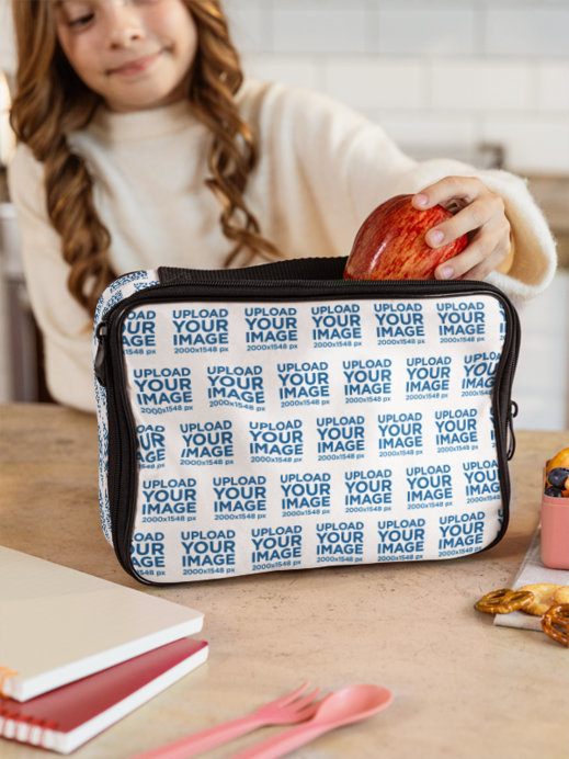 Lunch Bag Mockup featuring a Young Girl Putting an Apple Inside in a Kitchen Setting