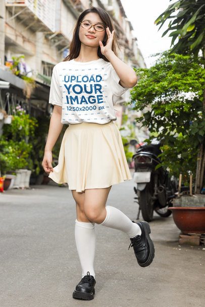 T-Shirt Mockup featuring a Young Woman in a K-Drama Style Outfit Adjusting Her Glasses on an Urban Street m55321
