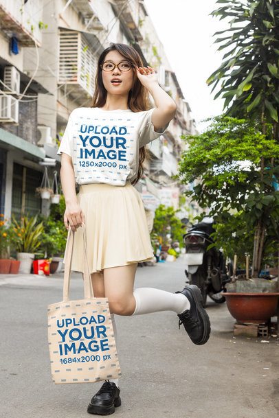 T-Shirt and Tote Bag Mockup featuring a Young Woman in a K-Drama Style Outfit Holding a Canvas Shopper on an Urban Street m55323