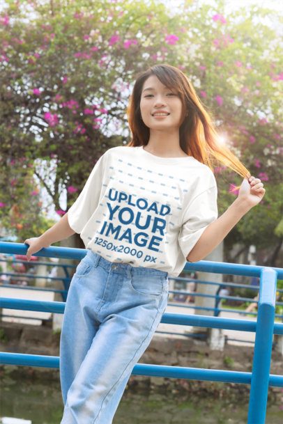 T-Shirt Mockup featuring a Smiling Young Woman with a K-Drama Style Holding Her Hair in an Outdoor Park Setting m55308