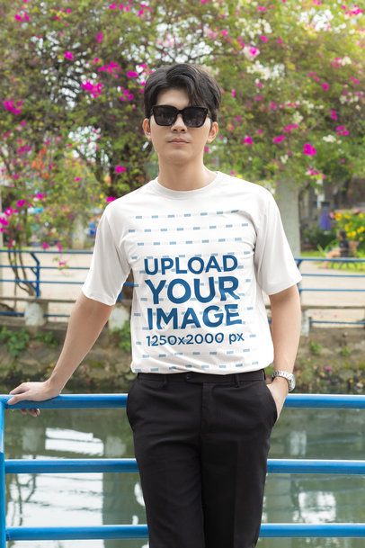 T-Shirt Mockup featuring a Cool Young Man with a K-Drama Vibe Leaning on a Blue Railing Outdoors m55306