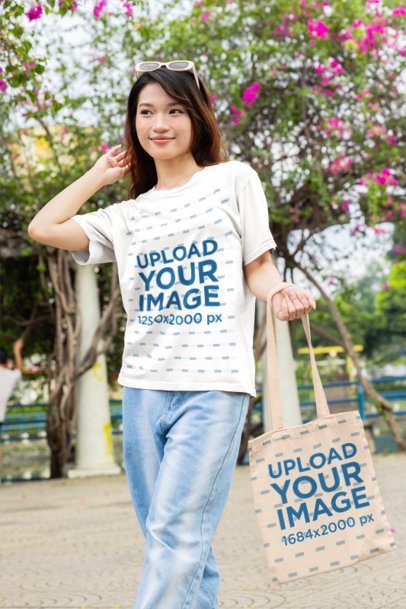 T-Shirt and Tote Bag Mockup featuring a young Asian woman holding her hair and walking in a park m55317