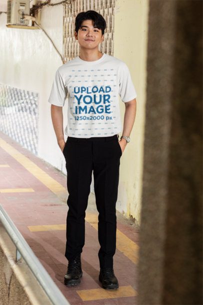 T Shirt Mockup featuring a Young K-Drama Male Lead Standing with Hands in Pockets in an Outdoor Corridor