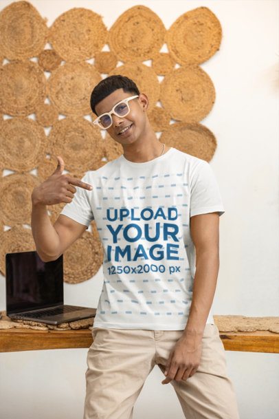 White T-Shirt Mockup of a Young Genzie Man with Glasses standing near a Laptop m55408