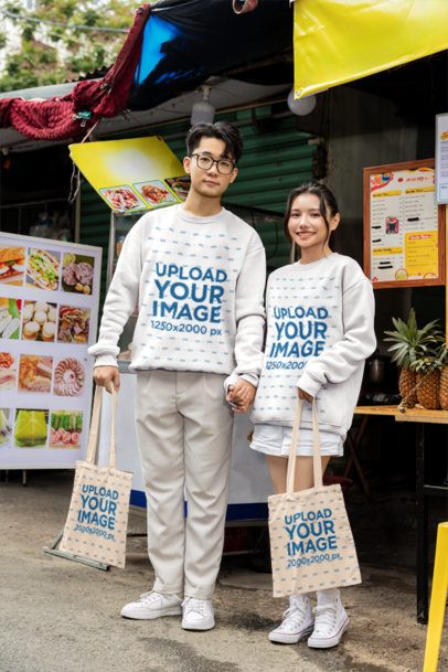 Sweatshirt and Tote Bag Mockup Featuring a Young Couple Holding Hands at a Street Food Stall