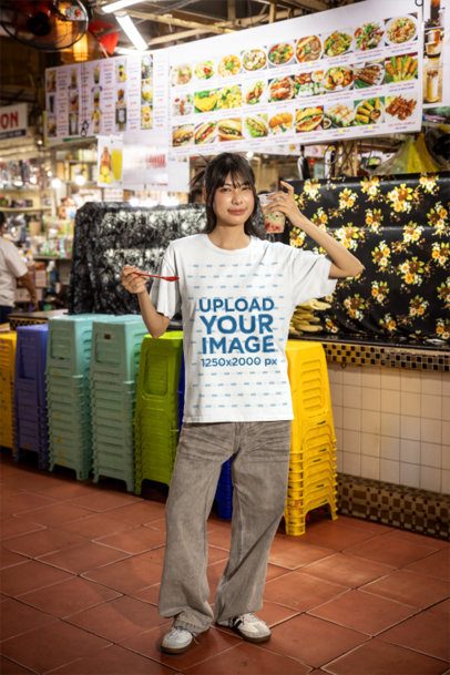 Shirt Mockup Featuring a Young Woman Holding a Drink and Spoon at an Asian Food Market