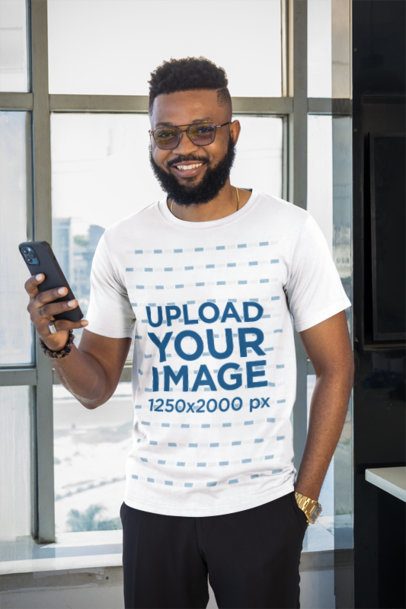 White Tee Mockup of a Bearded Man With Glasses Holding a Phone in a Modern High Rise